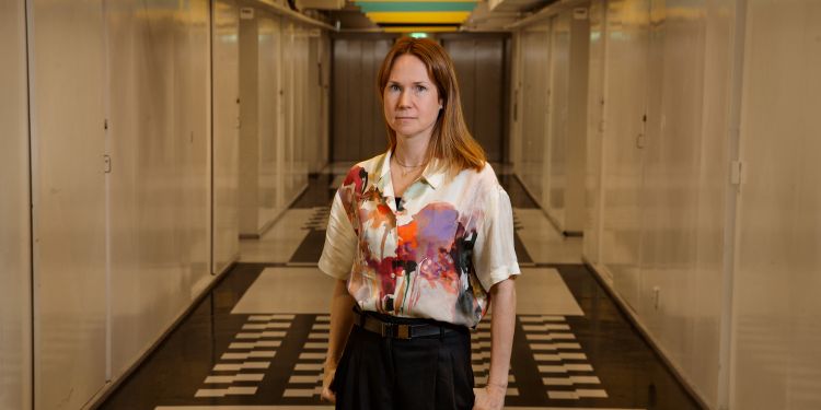 Kvinna med blommig skjorta står i en lång, ljus korridor.