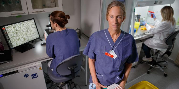 Kvinna i laboratoriemiljö håller en provplatta, andra forskare arbetar i bakgrunden.