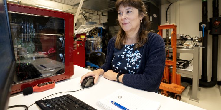 Kvinna sitter vid ett skrivbord framför en dator, omgiven av teknisk utrustning.