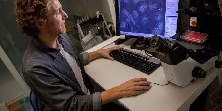 Man i laboratorium arbetar vid en dator med mikroskop och prover i bakgrunden.