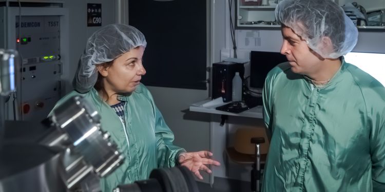 Två forskare i gröna labbrockar diskuterar i ett modernt laboratorium.