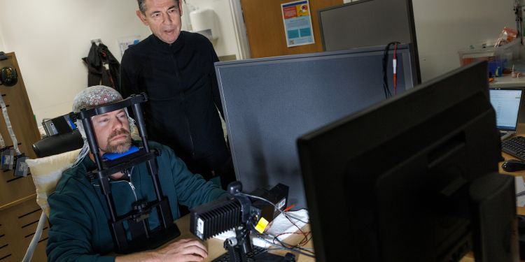 En man med hjälm arbetar vid en dator medan en annan man tittar över hans axel.