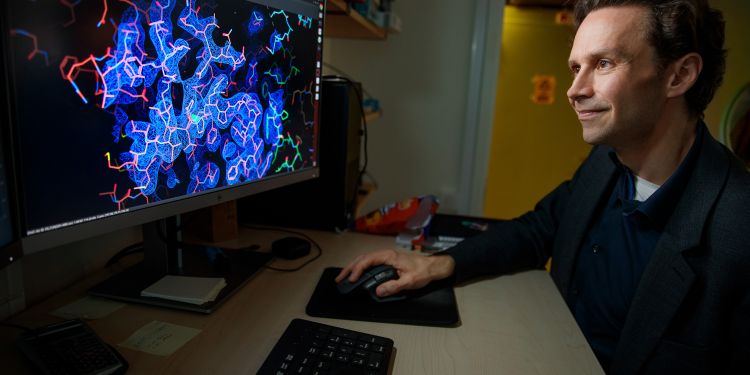 En man arbetar vid en dator med en färgglad molekylärstruktur på skärmen.
