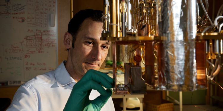 Forskare med gröna handskar inspekterar en komponent i ett laboratorium.