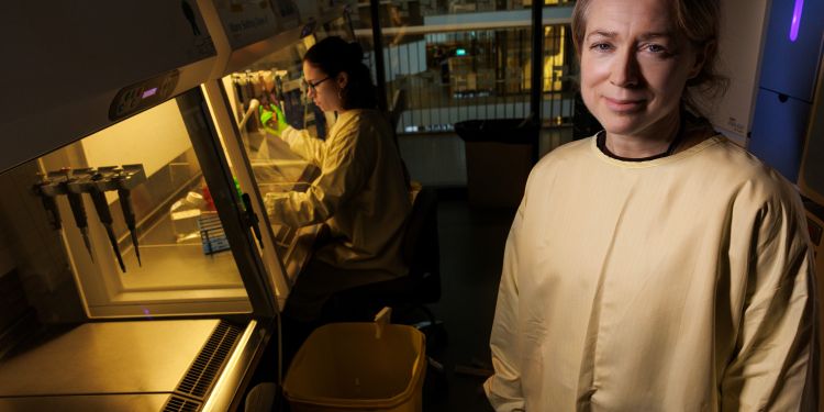 Kvinnlig forskare i ett laboratorium, klädd i skyddsdräkt, ler mot kameran.