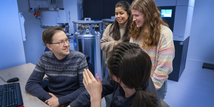 Fyra personer ler och pratar vid ett skrivbord i en labbmiljö.
