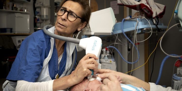 Sjuksköterska vårdar en nyfödd med medicinskt utrustning i ett sjukhusrum.