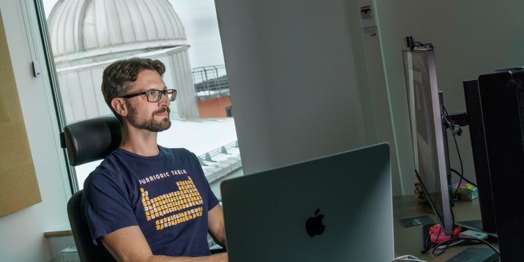 Man sitter vid skrivbordet framför en dator med observatorium i bakgrunden.