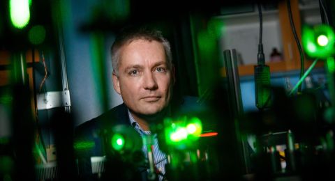 En man står framför en laboratoriemiljö med gröna ljus och optisk utrustning.