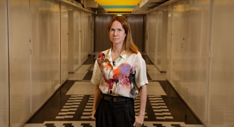 Kvinna med blommig skjorta står i en lång, ljus korridor.