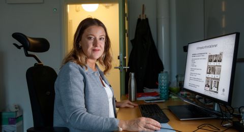 Kvinna sitter vid ett skrivbord med dator, ser fokuserad ut i ett kontor.