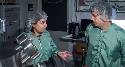 Två forskare i gröna labbrockar diskuterar i ett modernt laboratorium.