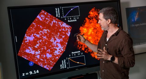 En man pekar på en stor skärm som visar röd och orange vetenskaplig data.