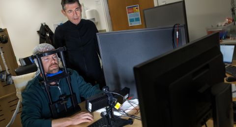 En man med hjälm arbetar vid en dator medan en annan man tittar över hans axel.