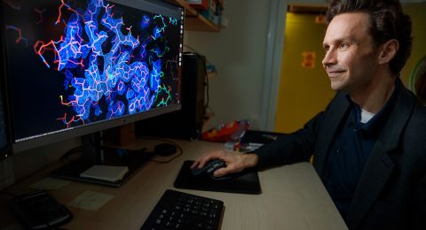 En man arbetar vid en dator med en färgglad molekylärstruktur på skärmen.