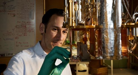 Forskare med gröna handskar inspekterar en komponent i ett laboratorium.