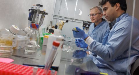 Forskare i labbrockar arbetar vid ett bord fullt med laborationsutrustning.