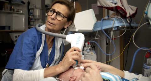 Sjuksköterska vårdar en nyfödd med medicinskt utrustning i ett sjukhusrum.