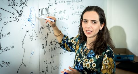 Kvinna skriver på en vit tavla täckt med matematiska formler och diagram.