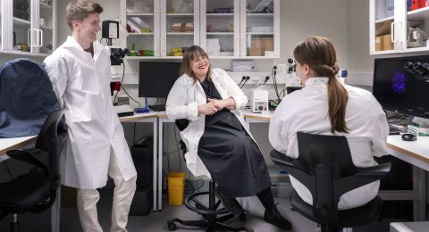 Tre forskare sitter och pratar i ett labb, omgivna av datorer och vetenskaplig utrustning.