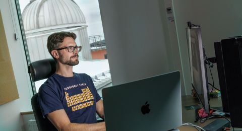 Man sitter vid skrivbordet framför en dator med observatorium i bakgrunden.